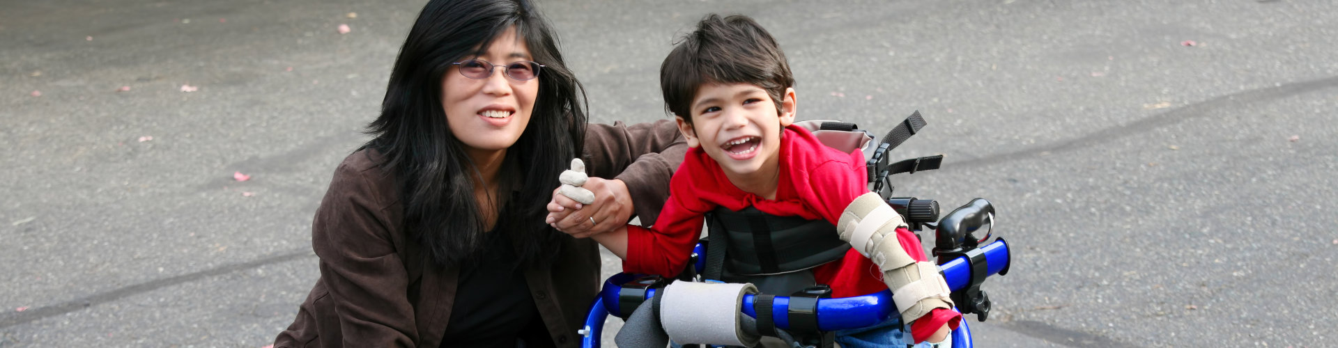 woman helping disabled child walk in his walker outdoors